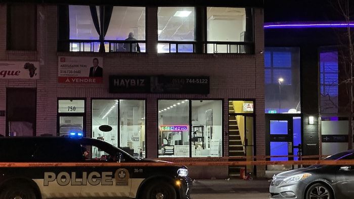 A commercial building whose second floor is lit, in the evening, and in front of which is parked a vehicle of the SPVM.