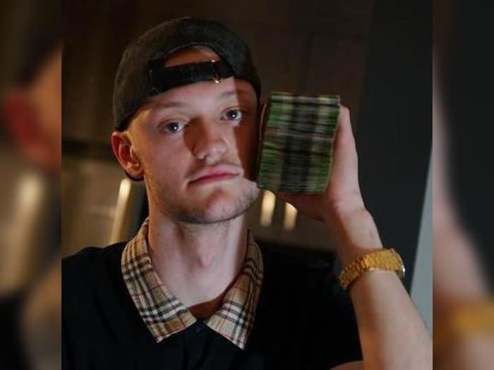 A young man with a cap holding a stack of banknotes.