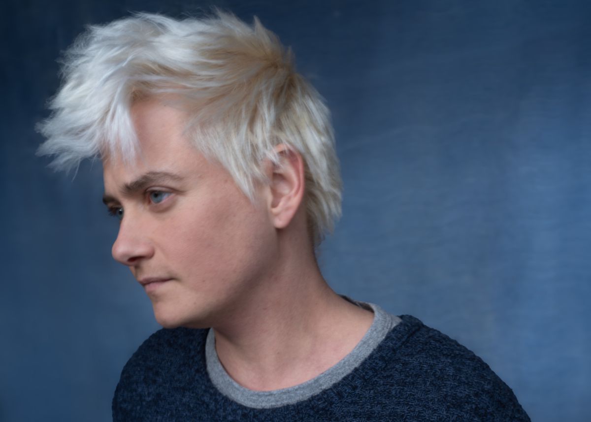 Person with blond and short hair looking to the left, wearing a gray sweater. Person with blond and short hair looking to the left, wearing a gray sweater.