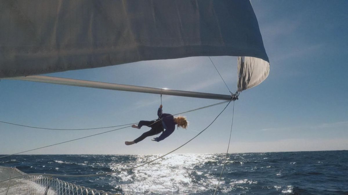Person hanging under a boat sail at sea on a sunny day. Person hanging under a boat sail at sea on a sunny day.