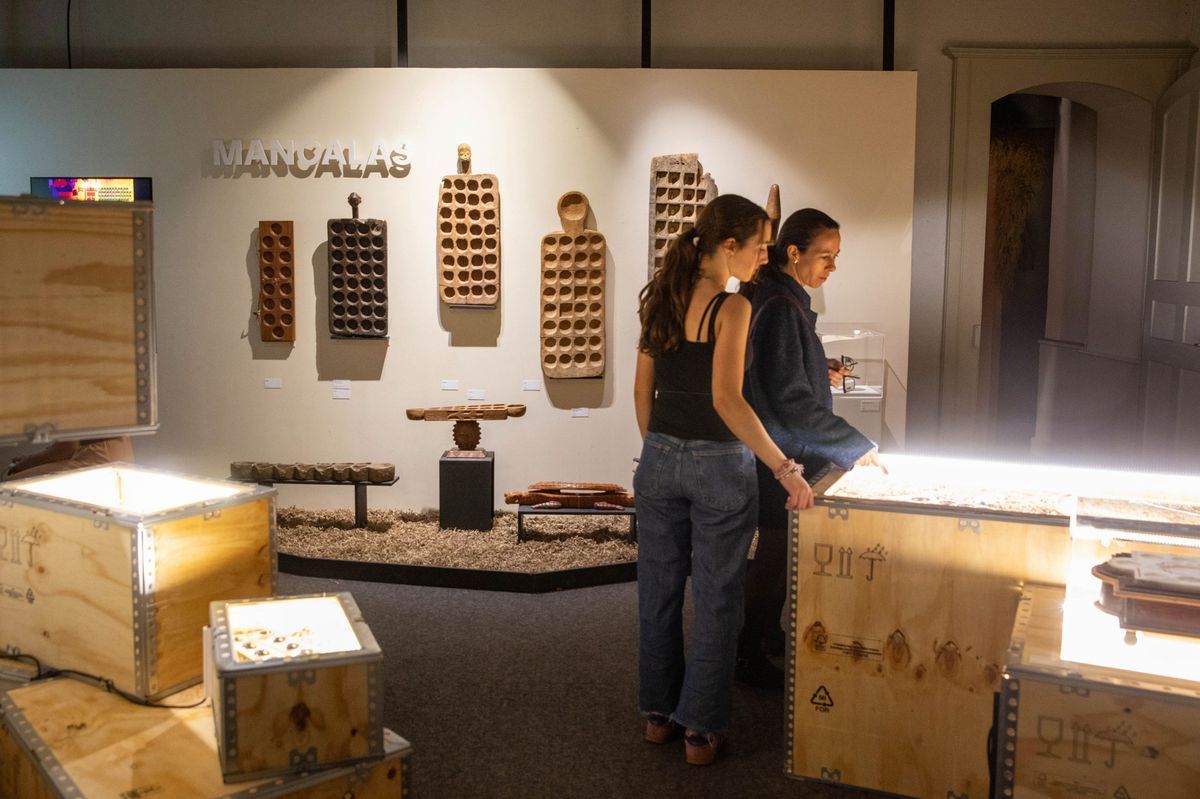 Two visitors explore an exhibition at the Swiss game museum, highlighting traditional Mancala games, with a light atmosphere and wooden displays. Two visitors explore an exhibition at the Swiss game museum, highlighting traditional Mancala games, with a light atmosphere and wooden displays.
