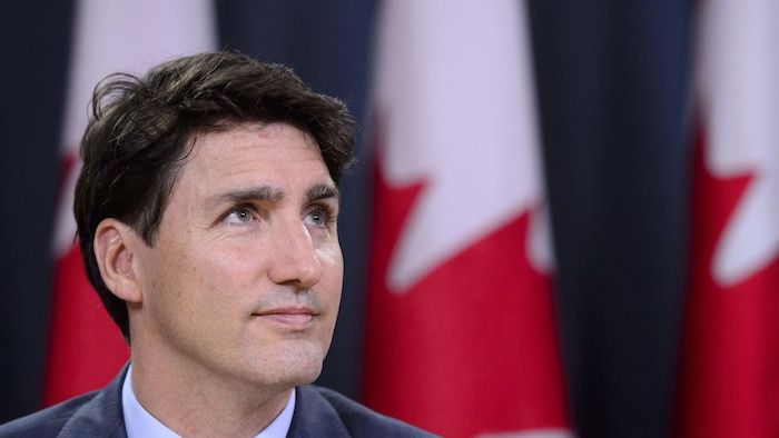Justin Trudeau at a press conference, in front of Canada flags.