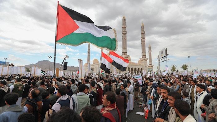 Yemenis brandish signs and flags from Yemen and Palestine during a gathering.