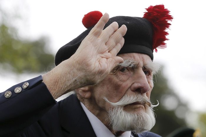 An 88 -year -old man in uniform, wearing a Bérêt, wearing a white mustache with curved ends, is a military salute.