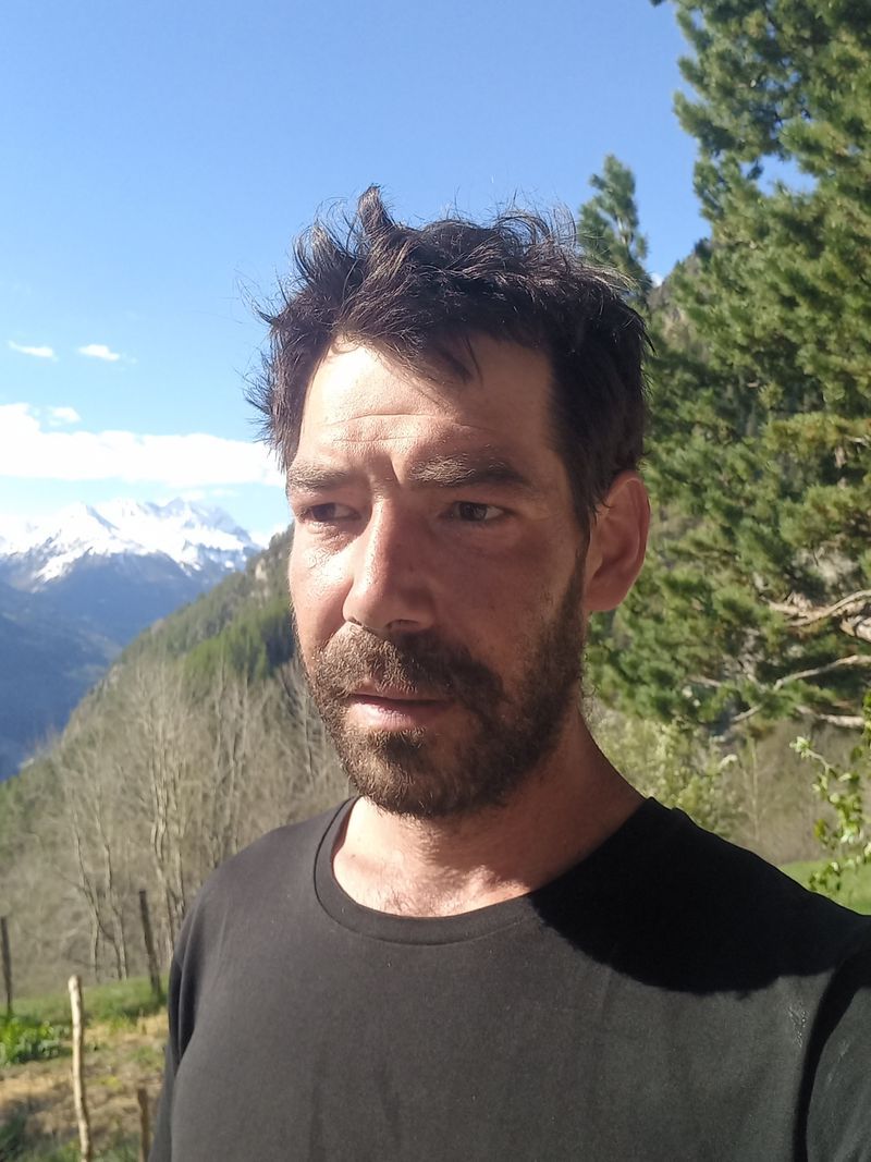 Bearded man in the open air, background of snowy mountains and green trees under a light blue sky. Bearded man in the open air, background of snowy mountains and green trees under a light blue sky.