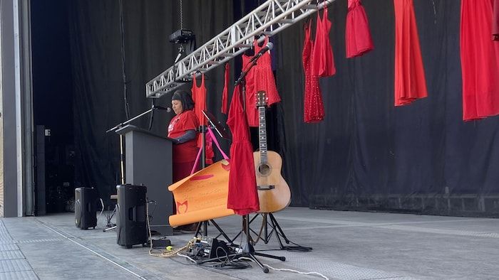 Juliette Wemigwans in front of a few red dresses, on the platform.