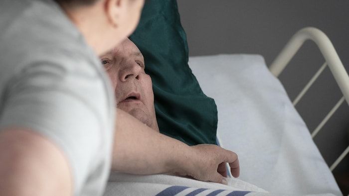 Normand Meunier, whose face is only seen in his hospital bed, with his spouse at her bedside.