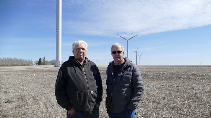 Two men in front of wind turbines.
