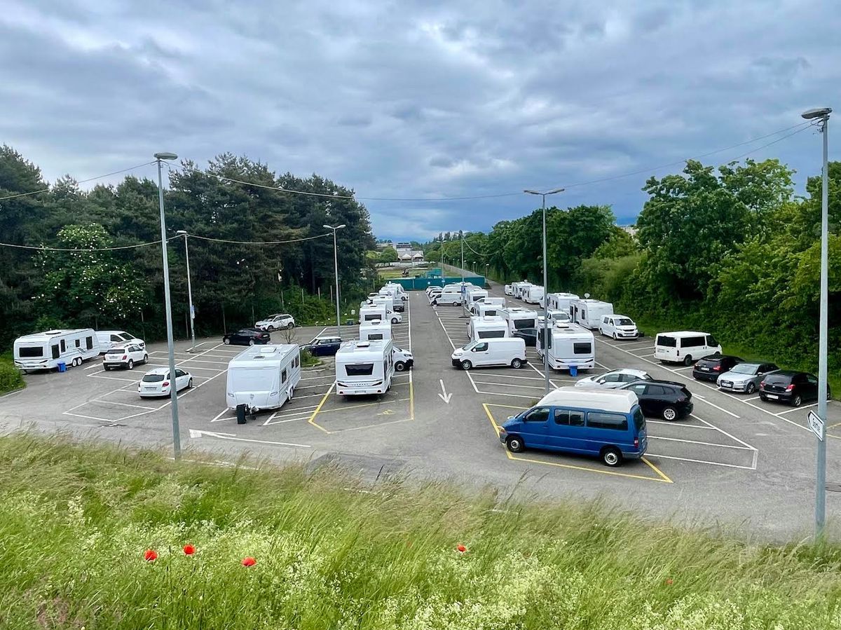 A parking lot filled with white caravans and cars, surrounded by trees and greenery under a cloudy sky. A parking lot filled with white caravans and cars, surrounded by trees and greenery under a cloudy sky.