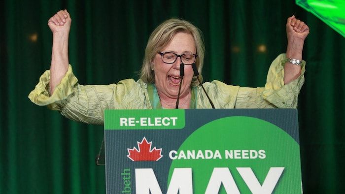 Elizabeth May speaks at the microphone and raises her arms as a sign of victory in the gallery on the evening of the elections.