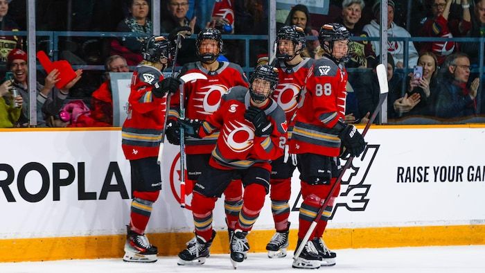 Hockey players in a red uniform are grouped after scoring a goal during a professional match.