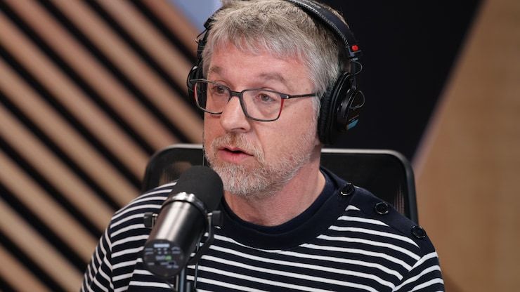 Patrick Kearney, head listening helmet, speaks in a microphone, in a radio studio.
