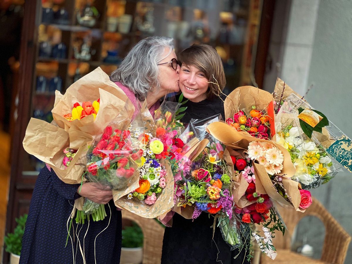 Two women in a joyful embrace holding large bouquets of colorful flowers in front of the Betjeman & Barton store in Carouge. Two women in a joyful embrace holding large bouquets of colorful flowers in front of the Betjeman & Barton store in Carouge.