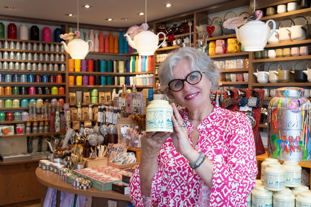 Smalling elderly woman, holding a tea jar, in a shop filled with teapots and colored cups on display on shelves. Smalling elderly woman, holding a tea jar, in a shop filled with teapots and colored cups on display on shelves.
