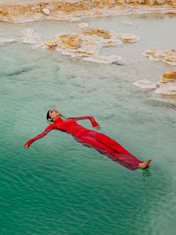 Person floating peacefully on clear water, dressed in a red combination, surrounded by white rock formations. Person floating peacefully on clear water, dressed in a red combination, surrounded by white rock formations.