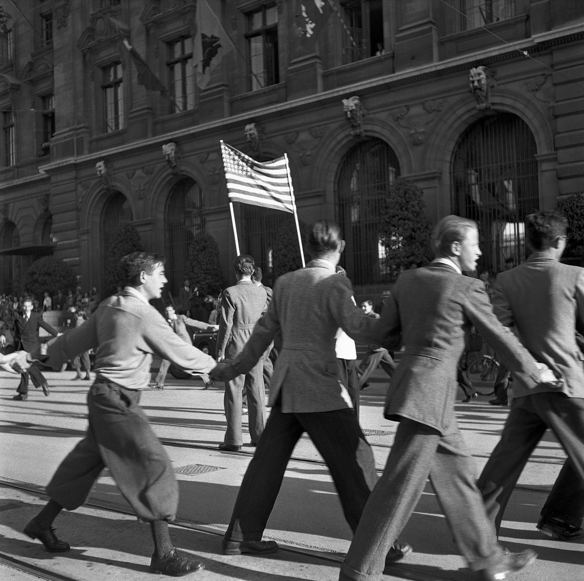People in Lausanne celebrate the end of the war on the street on May 8, 1945 with an American flag. The population dances exuberant while the buildings can be seen in the background. People in Lausanne celebrate the end of the war on the street on May 8, 1945 with an American flag. The population dances exuberant while the buildings can be seen in the background.