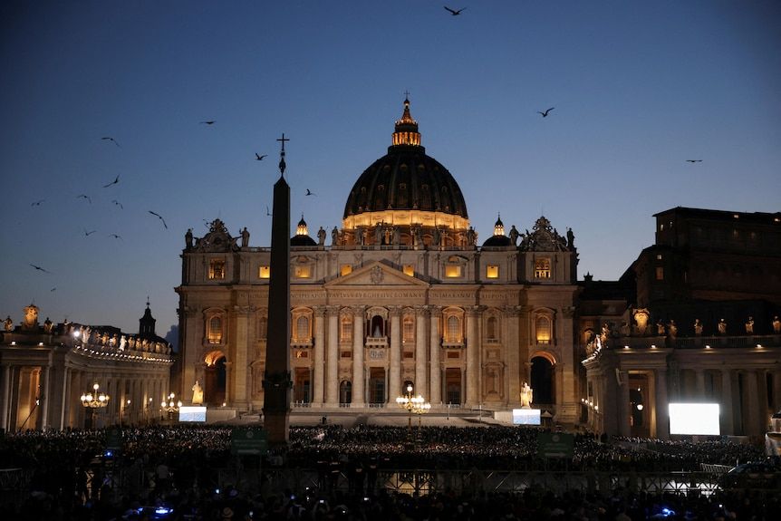 Crowds gathered in the dark in St Peter's Square at the Vatican as the sun sets over the Basilica