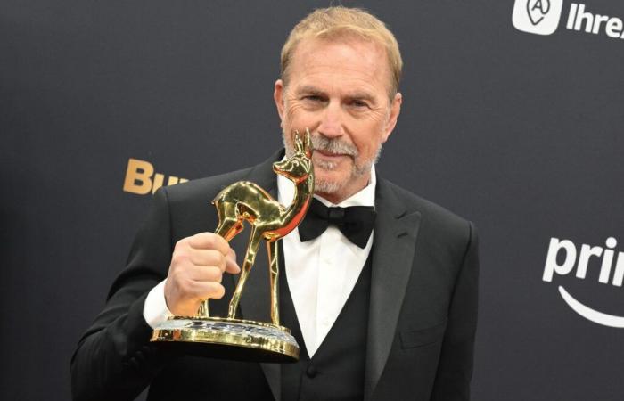 the actor holds up his award on the red carpet