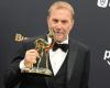 the actor holds up his award on the red carpet